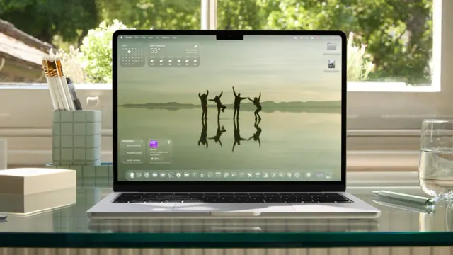 MacBook Pro on a glass desk showing macOS Tahoe in Apple’s June 2025 press image