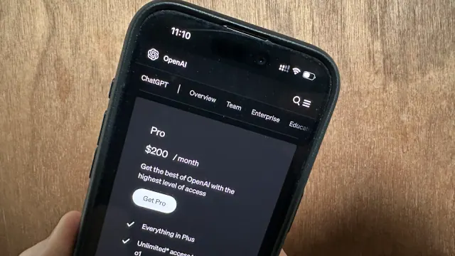A hand holds a smartphone displaying the ChatGPT Pro plan at $200 per month
